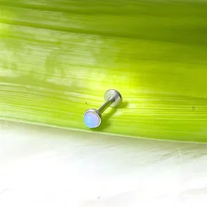 Dettaglio di un piercing labret in acciaio al titanio con opale blu su foglia verde