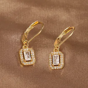 Close-up of golden rectangular drop earrings with zircon crystals on brown silk background