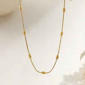 Minimalist gold snake chain necklace with oval beads shown against a soft beige background