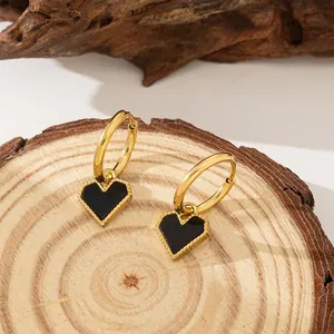 Detail shot of heart-shaped black pendant earrings on a gold-tone hoop over a wooden base