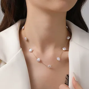 Elegante lange Goldperlenkette mit weißen Muschelperlen auf einem weißen Sakko getragen