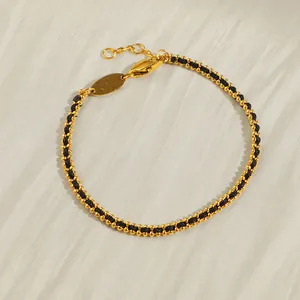 Detail eines geflochtenen schwarzen Armbands mit goldenen Perlen und Karabinerverschluss
