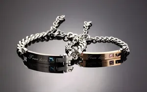 Detail of couple bracelets with True Love engraving and cross pendant on black background