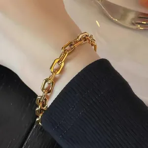 Detailansicht eines goldenen Büroklammer-Armbands am Handgelenk vor einem Esshintergrund