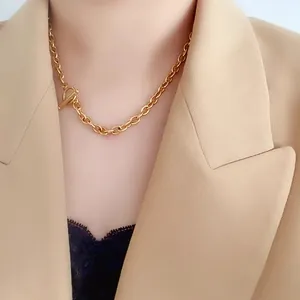 Close-up of gold OT buckle chain necklace worn with beige blazer and lace top