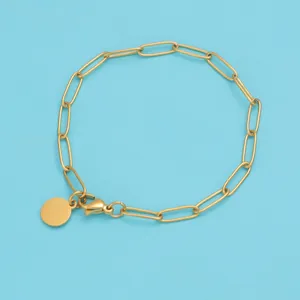 Close-up of golden paperclip chain bracelet with a polished round charm on blue background