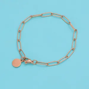 Detailed macro view of rose gold curb chain bracelet with circular charm on blue background