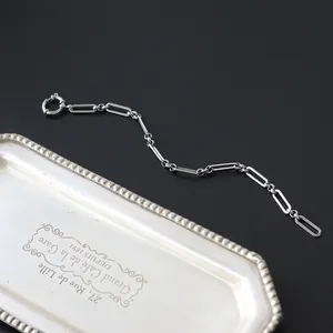 Detail von silberfarbenem Büroklammer-Kettenarmband mit Federringverschluss auf schwarzem Grund