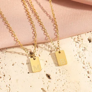 Detail of 18K gold plated square pendant necklaces with engraved letters M and B