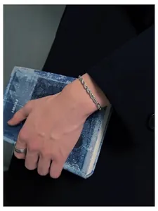 Close-up of a silver rope chain bracelet and hammered ring on a model in a black suit