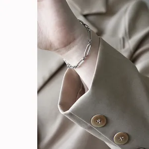 Minimalist silver steel paperclip chain bracelet worn on wrist with chic blazer