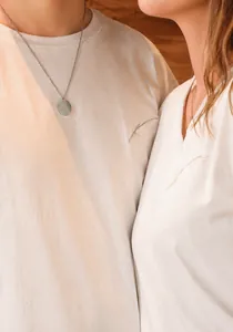 Close-up of minimalist round titanium steel pendant necklaces worn by a couple