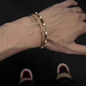 Dettaglio di bracciali a strati dorati con catena a corda e ciondoli a croce