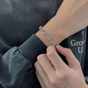 Bracelet chaîne argentée minimaliste avec nœuds porté sur la manche d'un pull gris