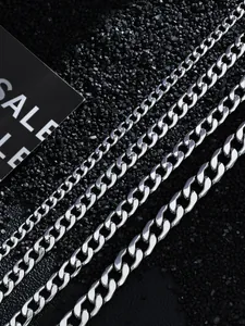 Detail view of four stainless steel Cuban link chains with mirror finish on stone background
