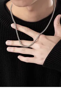 Detailed view of silver wheat chain necklace on a black knitted background