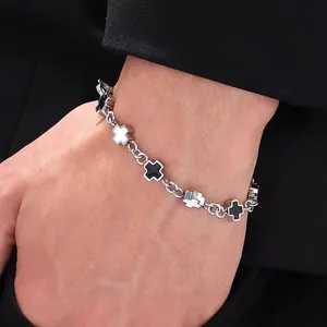 Detail of silver chain bracelet with black and white cross charms on dark suit sleeve