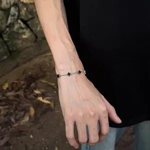 Close-up of titanium steel cross bracelet on wrist showing black enamel charms and silver chain