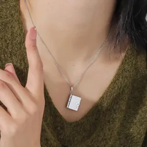 Polished silver heart book locket pendant necklace on green knit sweater
