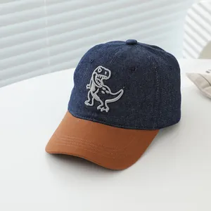 Close-up of children's denim baseball cap featuring detailed dinosaur embroidery and brown brim