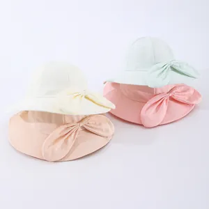 Flat lay of wide brim kids sun hats with large bows in beige, pink, and mint green