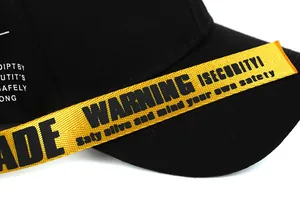 Dettaglio cappellino nero con cinturino giallo con testo WARNING e texture intrecciata