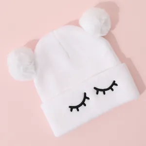Dettaglio del cappello in maglia bianca con ricamo a ciglia e doppi pompon in finta pelliccia