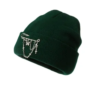 Detail of dark green knit beanie with silver chain, butterfly and cross punk ornaments