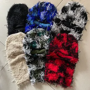 Flat lay view of various distressed balaclava hats with long tassel fringe and camo patterns