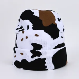 Knitted beanie hat with black and brown cow print pattern on white background