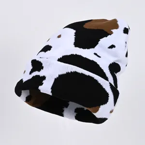 Knitted beanie hat featuring cow print pattern in black brown and white colors