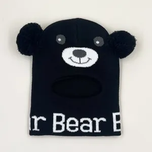 Dettaglio del passamontagna in maglia nera per bambini con motivo orso e doppi pompon