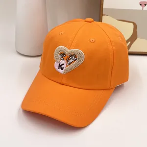 Détail d'une casquette orange avec broderie de dessin animé en cœur et la lettre K