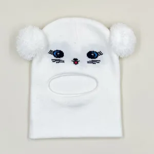 Close-up of white knitted baby balaclava with cat face embroidery and dual pom poms