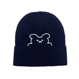 Dettaglio del berretto in maglia a coste blu navy con ricamo di orsetto bianco sul risvolto