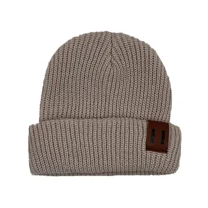 Detailed view of the thick ribbed knit texture and brown faux leather patch on the beanie