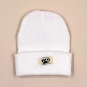 Close-up of white knitted beanie with MAMA'S MINI woven label on the folded brim