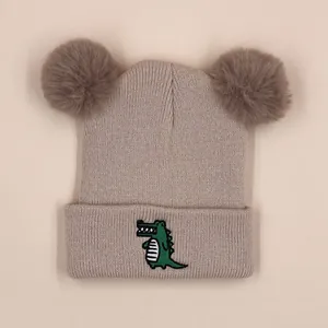 Beige knitted baby beanie with cute green crocodile embroidery and double pom-poms