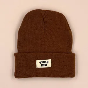 Deep brown knitted beanie for toddlers featuring a Mama's Mini patch on a pink background