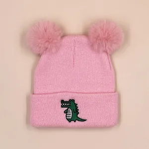 Pink knit baby beanie with cute green crocodile embroidery and dual faux fur pom-poms