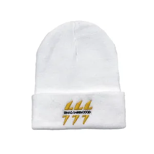 Détail de la broderie jaune avec texte LLL et 777 sur un bonnet en tricot blanc