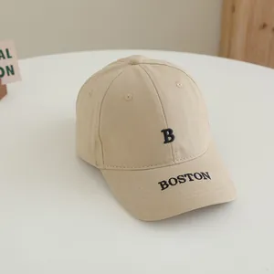 Détail d'une casquette en coton beige avec broderie BOSTON noire sur une table blanche