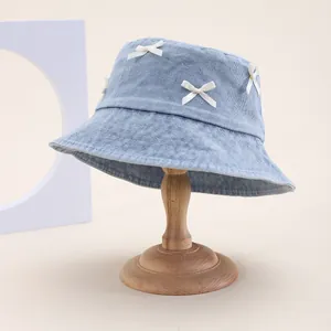 Chapeau bob en jean bleu clair avec nœuds blancs sur support minimaliste en bois