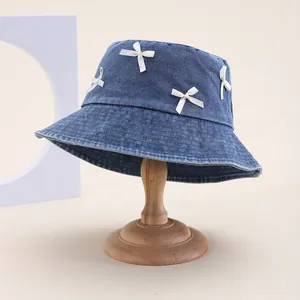 Chapeau bob en denim bleu avec quatre nœuds blancs sur un support en bois épuré