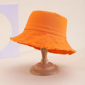 Dettaglio dei bordi sfrangiati su un cappello a secchiello in tela arancione acceso
