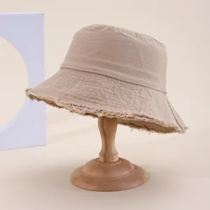 Cappello a secchiello beige da donna con bordo sfrangiato su supporto in legno