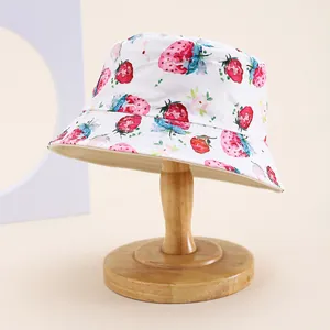 Détail de l'imprimé fraises et fleurs sur un chapeau bob blanc en coton pour enfants