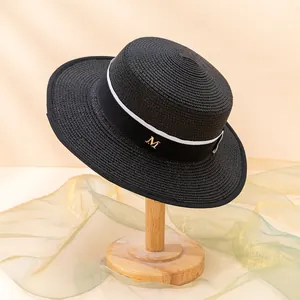 Detailaufnahme des schwarzen Strohhutes mit schwarz-weißem Band und goldenem M-Logo