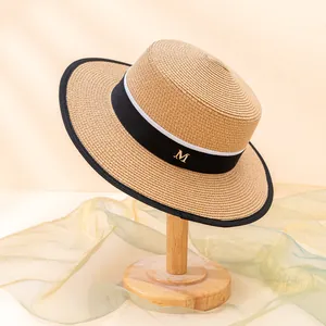 Eleganter flacher Strohhut mit schwarzem Band und goldenem M-Metallemblem-Detail