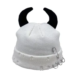 Detail of cream knit beanie with black devil horns, safety pin and punk rings